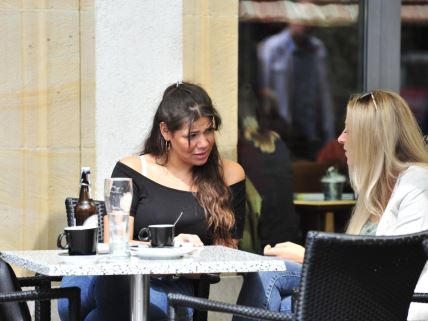 Dve žene sede u bašti kafića i razgovaraju