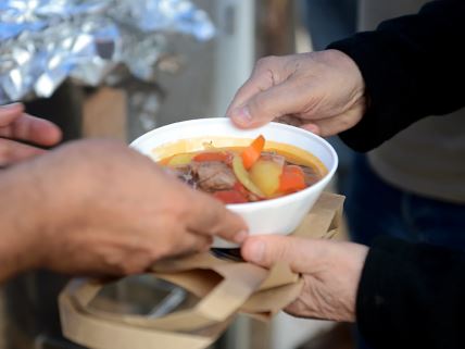 Ruke drže belu činiju sa čorbom i povrćem iznad papirne kese