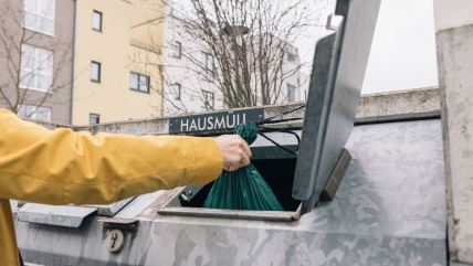 Ruka drži smeće koje ubacuje u kontejner