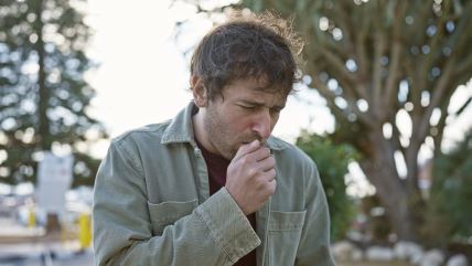 Muškarac kašlje u parku, sa zelenilom u pozadini