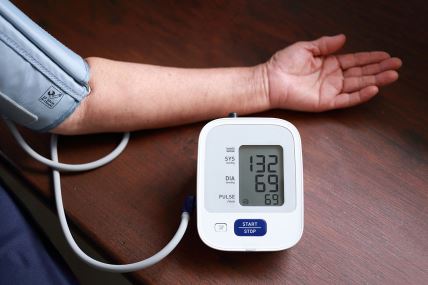 Ruka sa manžetnom za merenje krvnog pritiska na drvenom stolu.