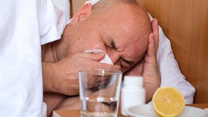 Čovek duva nos u maramicu pored lekova, čaše vode i limuna