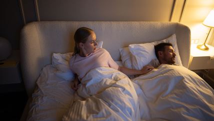 Žena u krevetu gleda muškarca dok spava