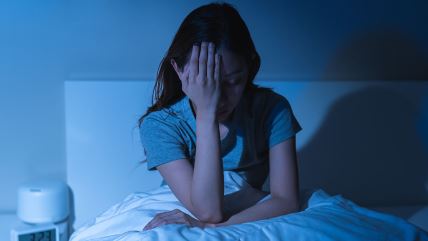 Žena se drži za glavu u krevetu