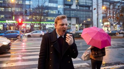 Muškarac sa kafom u ruci zeva na ulici