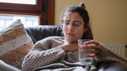Devojka sa naočarima se drži za grlo dok drugom rukom uzima čašu sa vodom