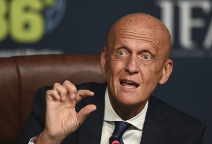 Pjerluiđi Kolina pokazuje rukama, dok sedi u odelu.