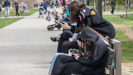 Tinejdžerke sa telefonima u rukama na klupici u parku