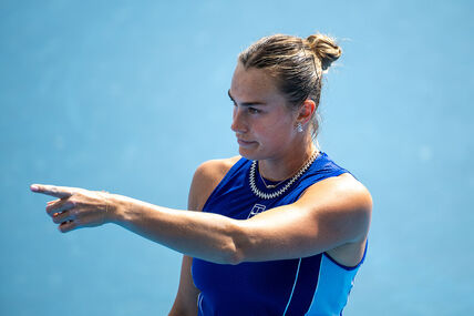 Arina Sabalenka pokazuje prstom dok je iza nje plava pozadina.