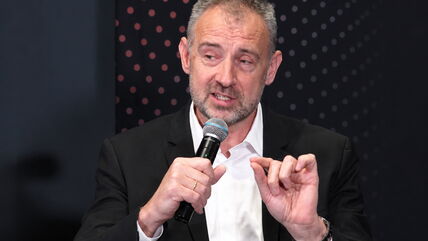 Nikola Grbić drži mikrofon i govori na panelu dok je obučen u crno odelo i belu košulji.