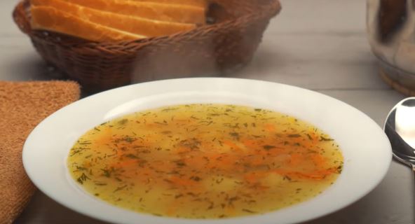 Bistra posna supa od povrća u belom tanjiru na stolu i korpa sa hlebom