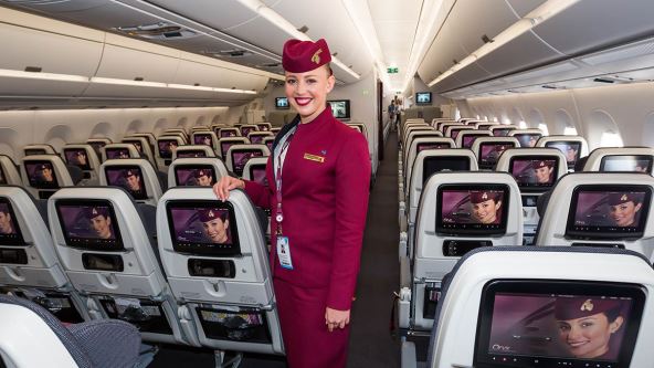 Stjuardesa avio-kompanije Qatar Airways stoji između sedišta u avionu.