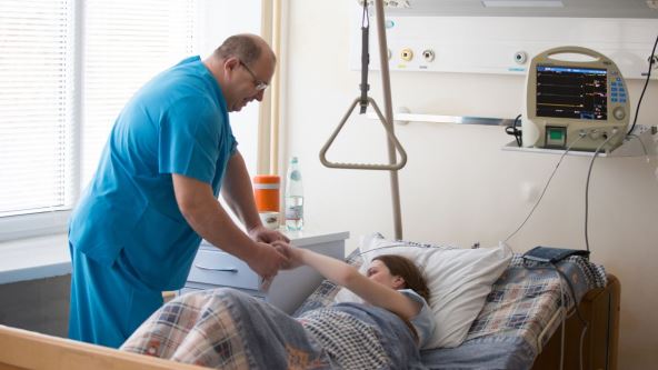 Medicinski radnik pomaže pacijentkinji u bolničkom krevetu