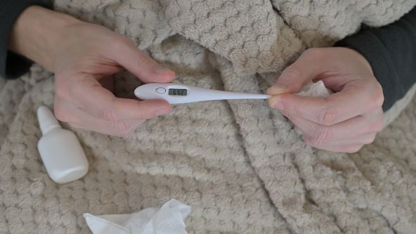 Toplomer u rukama, sprej za nos i maramice na krevetu