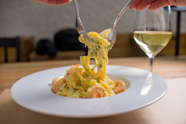 Karbonara pasta u tanjiru i čaša belog vina u pozadini