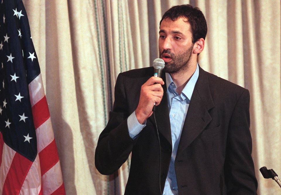 Vlade Divac sa mikrofonom pored američke zastave.